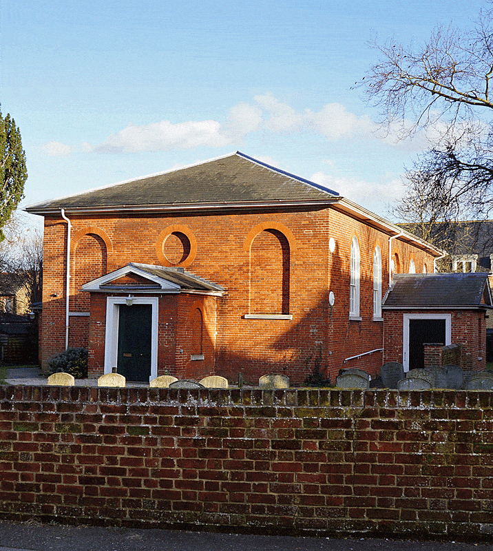 The Meeting House is 1.5 stories high, is shaped as a rectangular, and has a hip roof. The trim is white. The windows are tall with round tops. There are no windows on the front façade but bricks are recessed in the shape of windows. The entry is an enclosed porched with a gable roof.